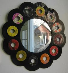 a round mirror with many different colored discs on it's side hanging on the wall