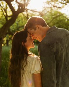 a young man and woman standing next to each other in the grass with trees behind them