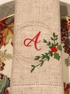 an embroidered napkin on top of a plate with holly and red berries in the center