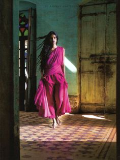 a woman in a pink dress is walking through an open doorway with her hair blowing in the wind