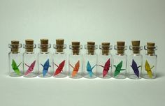 six glass bottles with different colored paper birds in them, all lined up on top of each other