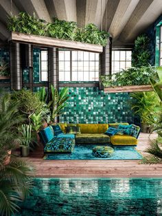 a living room filled with lots of green plants and furniture next to a swimming pool