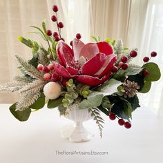 a vase filled with flowers and greenery on top of a white table next to a window