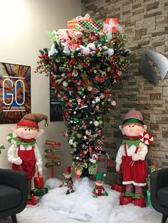 two christmas decorations in the shape of elves and elfs next to a decorated tree