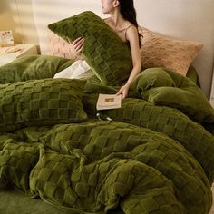 a woman sitting on top of a bed covered in green comforter and two pillows