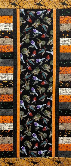 a quilted wall hanging on the side of a wooden fence with orange and black strips