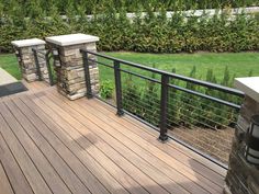 a wooden deck with stone pillars and railings next to a grassy area in the background