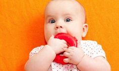 a baby holding a red object in its mouth