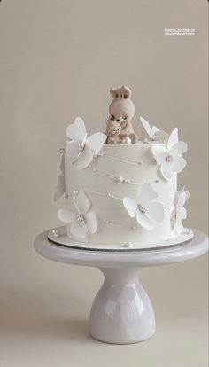 a white cake with butterflies and a teddy bear on top