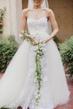 a woman wearing a wedding dress and holding a bridal bouquet in front of her