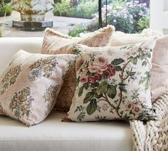 a white couch with pillows on top of it next to a vase and window in the background