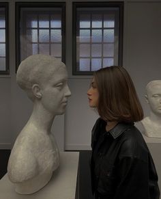 a woman standing next to a white busturine in an art gallery looking at it