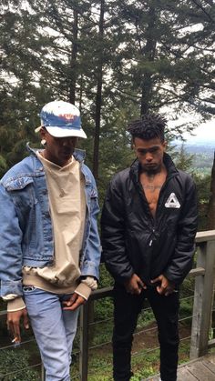 two men standing next to each other on a wooden deck in front of some trees