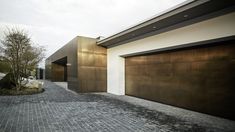 two brown garage doors on the side of a white and black house with brick driveway