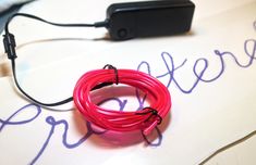 a red wire connected to a black device on top of a white table with writing underneath it