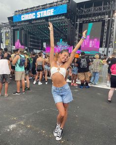 a woman dancing in front of a crowd at a music festival with her arms up