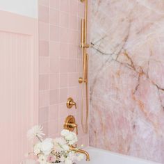 a bathroom with pink marble walls and gold fixtures, white flowers in the bathtub