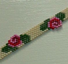 a beaded bracelet with pink flowers and green leaves on the end, sitting on a white surface