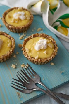 three small pies with whipped cream on top are sitting next to a fork and napkin