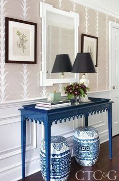 a blue and white table with two vases on top of it next to a mirror