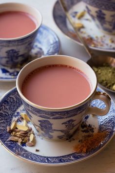 two cups of tea on a saucer with spoons next to it and spices