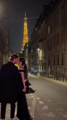 a man and woman kissing in front of the eiffel tower at night time