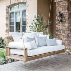 a porch swing with pillows on it in front of a house