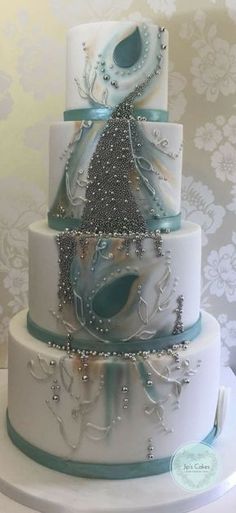 a three tiered wedding cake decorated with blue and white frosting, beaded decorations