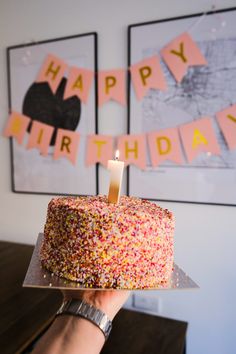 a person holding up a birthday cake with a candle on it