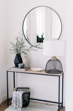 a table with a mirror, vase and lamp on it in front of a white wall