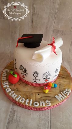 a cake decorated with an apple and graduation cap on a wooden platter that says congratulations miss