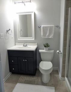 a white toilet sitting next to a sink in a bathroom under a mirror and towel rack