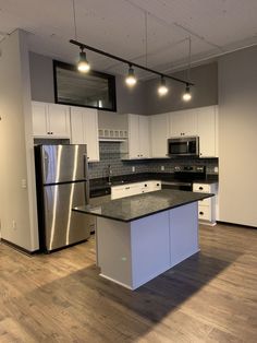 an empty kitchen with stainless steel appliances and black counter tops, white cabinets and wood flooring