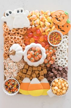 an assortment of halloween treats arranged on a white surface with pumpkins, pretzels and candy