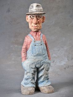 an old figurine wearing overalls and a hat is posed in front of a gray background