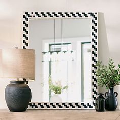 a mirror sitting on top of a wooden table next to a lamp and vases