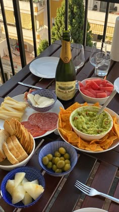 a table with plates and bowls of food on it, including breads, crackers, olives, tomatoes, and cheese