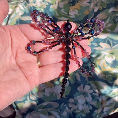 a person is holding a beaded spider in their hand