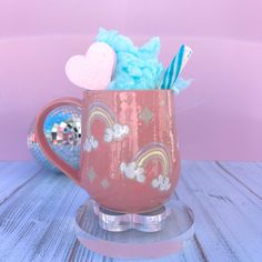 a pink coffee mug with some blue and white stuff in it on a stand next to a mirror