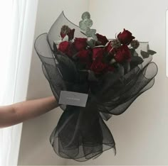 a person holding a bouquet of red roses in their left hand with the tag on it