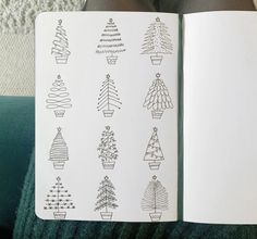 an open book with christmas trees drawn on it's pages and in front of someones legs