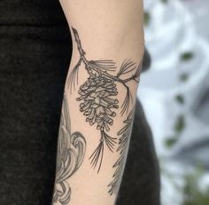 a woman with a tattoo on her arm holding a pine cone and branch in the background