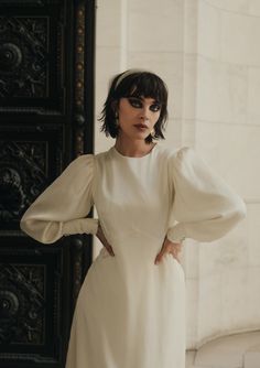 a woman standing in front of a door wearing a white dress with puffy sleeves