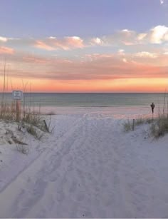 an empty beach with sand and sea oats at sunset in the foreground, there is a sign that says no swimming here