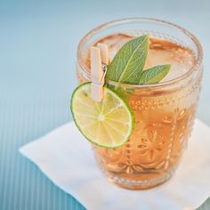 a glass filled with ice and lime on top of a napkin