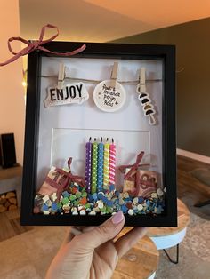 a person holding up a shadow box filled with birthday candles and personalized magnets