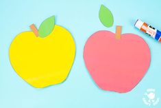 two apples cut out with colored paper and glue on a blue background next to an orange marker