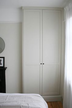 a bedroom with white walls and wooden flooring, an armoire is next to the bed