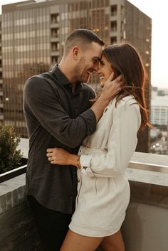 a man and woman standing next to each other on top of a roof in front of tall buildings