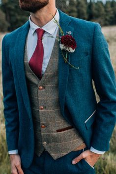 a man wearing a suit and tie with a flower in his lapel, standing in a field